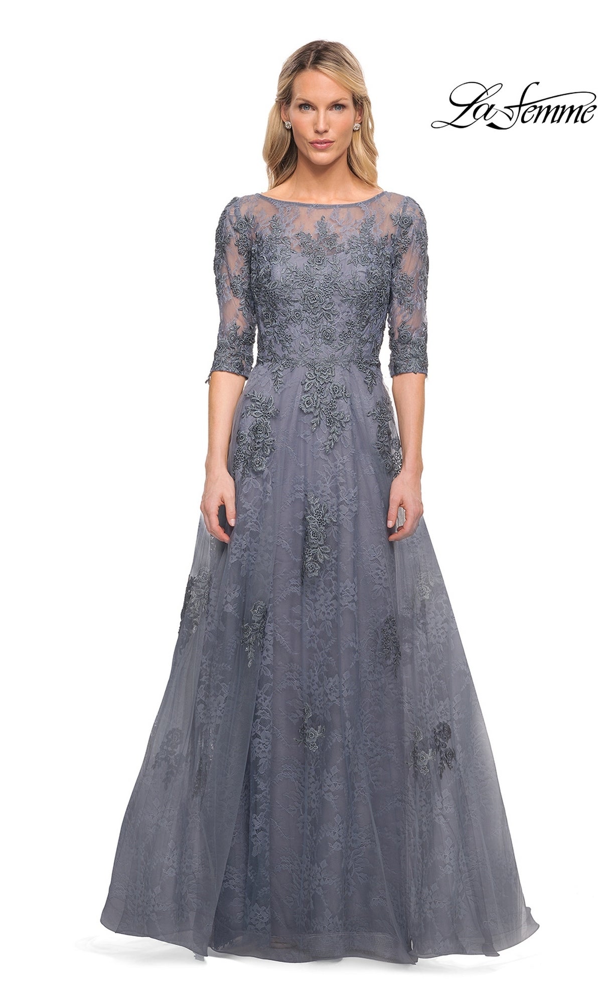 A woman wearing the Long Formal Dress: La Femme 28036 in slate with floral lace appliqué and half sleeves stands against a white background.